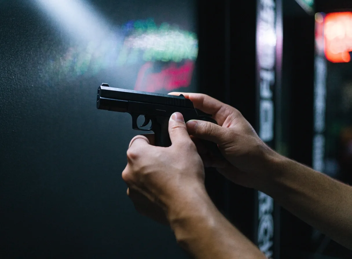 Duas mãos segurando uma pistola de brinquedo na altura do peito sob holofote frio