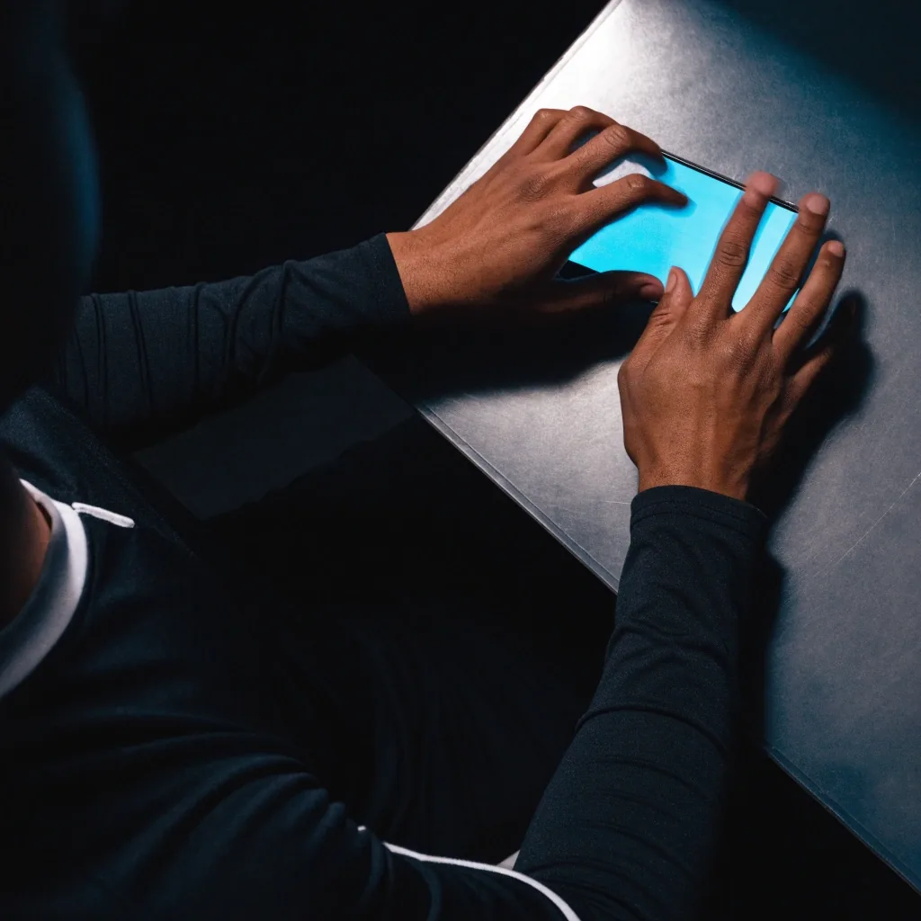 Mãos de um jogador em movimento sobre o teclado, iluminadas pelo brilho frio da tela em um quarto escuro