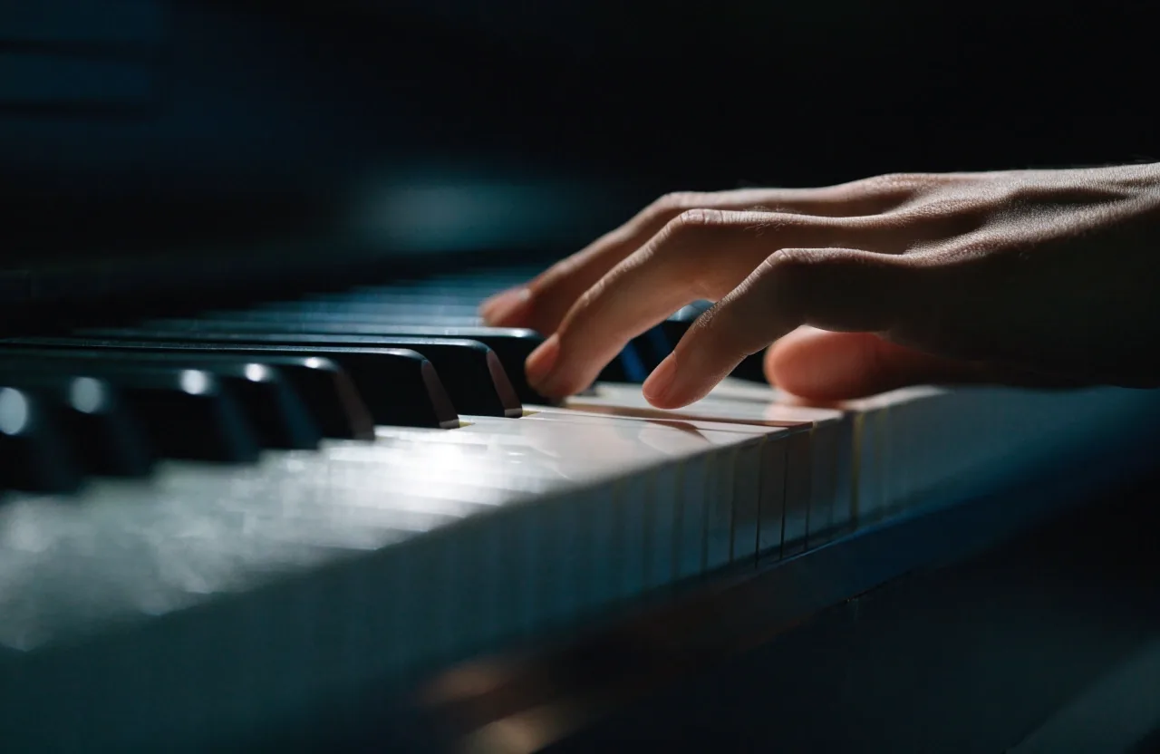 Pontas dos dedos tocando as teclas iluminadas de um piano vertical no escuro